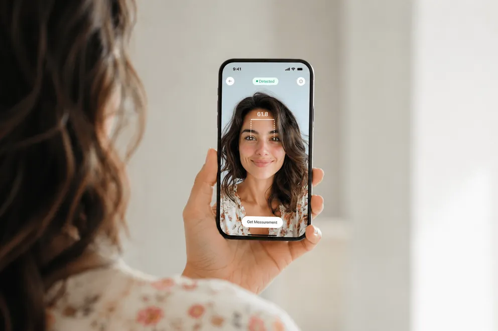 Una mujer sostiene un iPhone con el brazo extendido mientras una app de DP mide en la pantalla la distancia entre sus pupilas